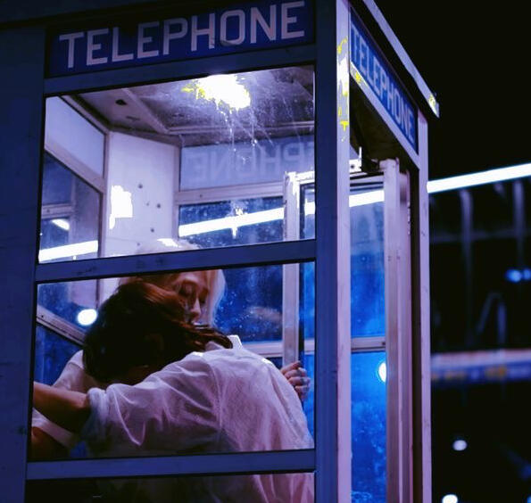 A picture in blue and purple showing Kyubin and Yoojung from the K-pop group OnlyOneOf leaning against each other in a telephone cell. This screenshot is from the music video of “begin” by Yoojung of OnlyOneOf.